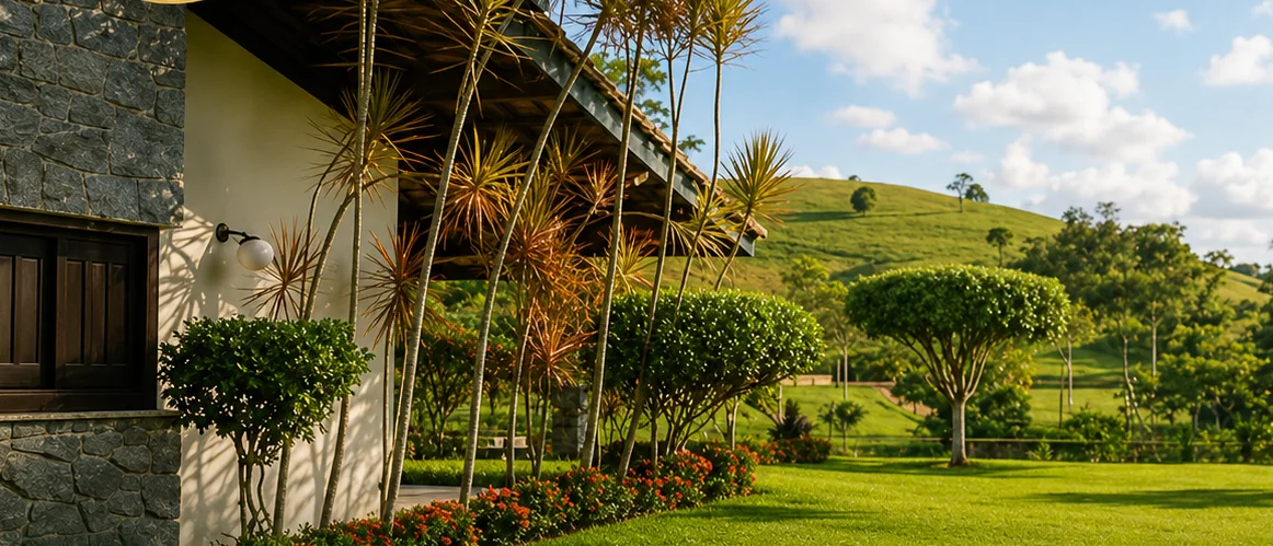 Lateral da casa-sede em pedra, com jardim e morros verdes ao fundo